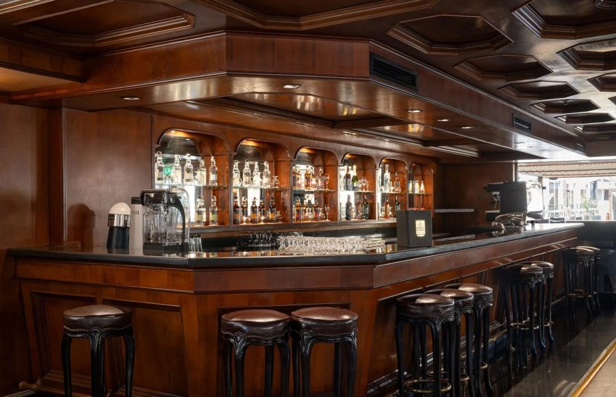 Angled view of the elegant MS Nile Plaza bar, showing the rich, polished wood counter, tiered bottle display, and brown leather bar stools.