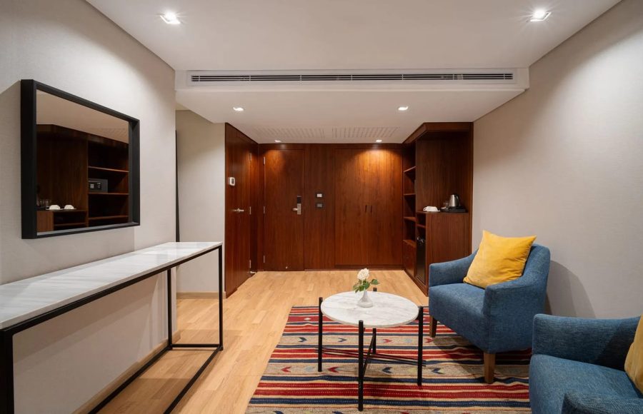 Living area of a Nile cruise suite featuring blue armchairs, a patterned rug, dark wood paneling, and a white marble console table.