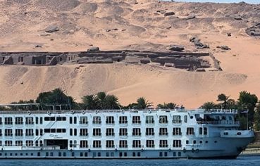 A close-up view of the MS Quest Nile Cruise ship in front of ancient Egyptian rock-cut tombs.
