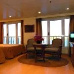 A bright guest cabin on the MS Quest featuring twin beds with velvet rust-colored runners and large drapes.