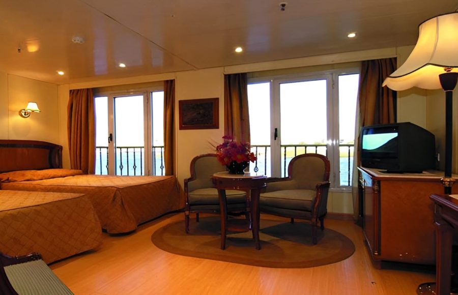A bright guest cabin on the MS Quest featuring twin beds with velvet rust-colored runners and large drapes.