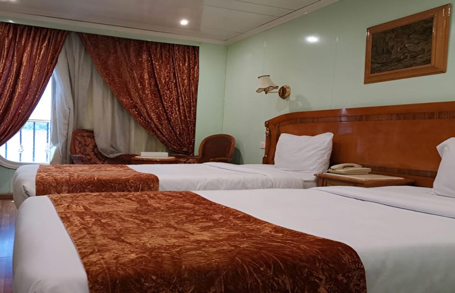 A traditional twin-bed cabin on the MS Quest Nile Cruise with large windows and a small seating area.