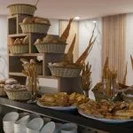A buffet display featuring a tiered wooden shelf with various breads and pastries organized in woven baskets.