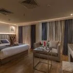 Deluxe cabin with a large bed, sofa, glass coffee table, and a desk/vanity with a flat-screen TV and welcome drinks.