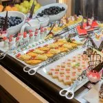 Close-up of a lavish dessert and fruit buffet featuring small cakes, individual parfaits, mango tarts, and bowls of dark grapes.
