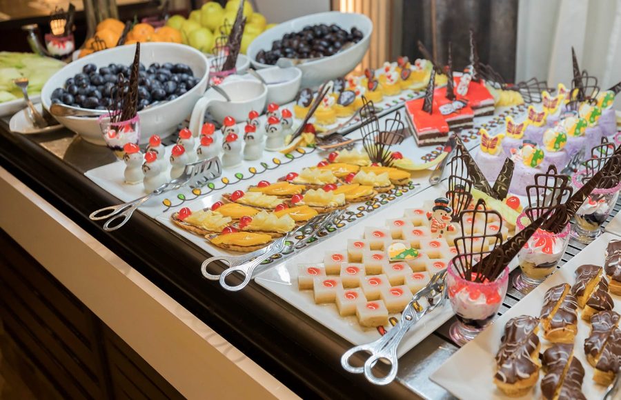 Close-up of a lavish dessert and fruit buffet featuring small cakes, individual parfaits, mango tarts, and bowls of dark grapes.