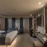 Luxury cabin with a large bed decorated with a towel swan, a seating area, a dressing table, and a wall-mounted TV.