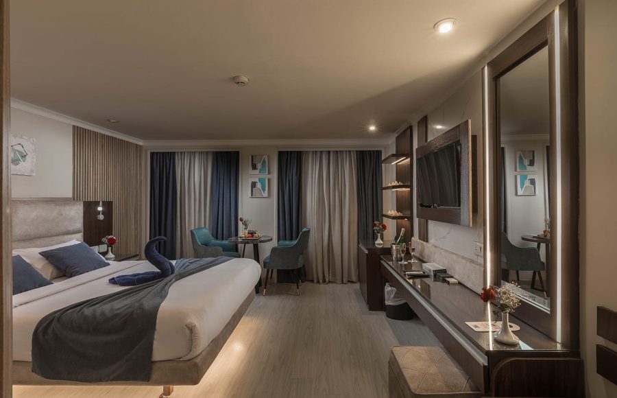 Luxury cabin with a large bed decorated with a towel swan, a seating area, a dressing table, and a wall-mounted TV.