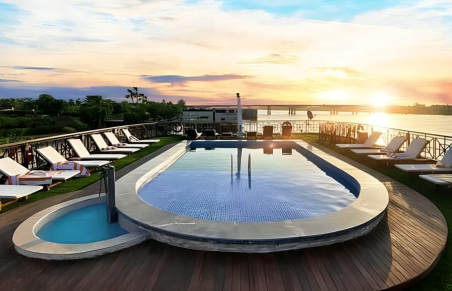 Rooftop pool and sun deck on a cruise ship at sunset, overlooking a river.