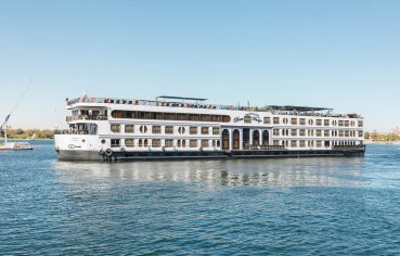 Side view of the white MS Royal Beaurivage Nile cruise ship with multiple decks and rows of windows, sailing on calm blue water under a clear sky.