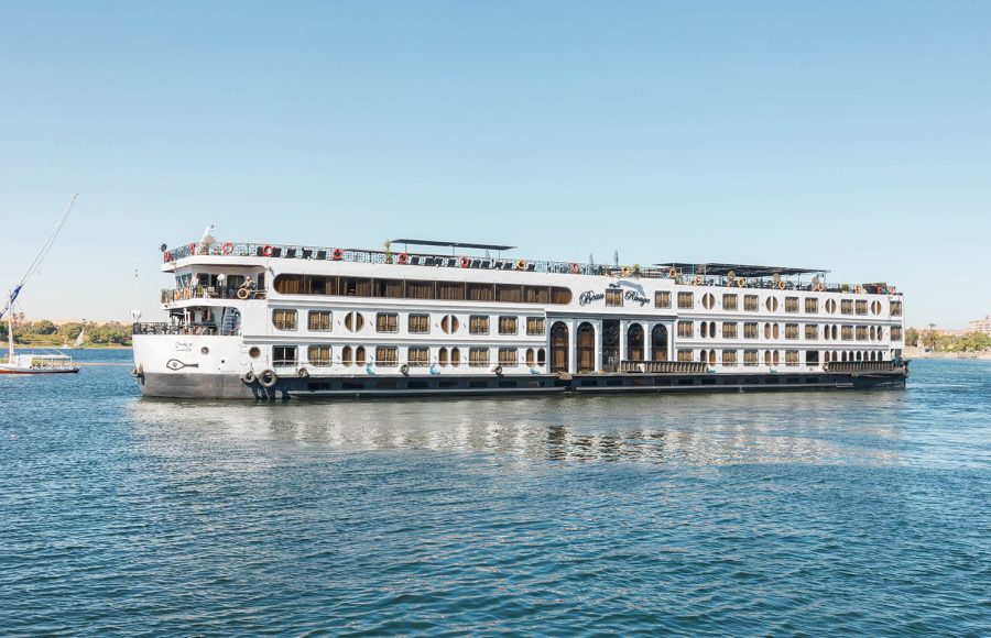 Side view of the white MS Royal Beaurivage Nile cruise ship with multiple decks and rows of windows, sailing on calm blue water under a clear sky.