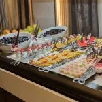 Buffet table featuring a rich array of colorful desserts, pastries, small cakes, and fresh fruit like grapes and melon.