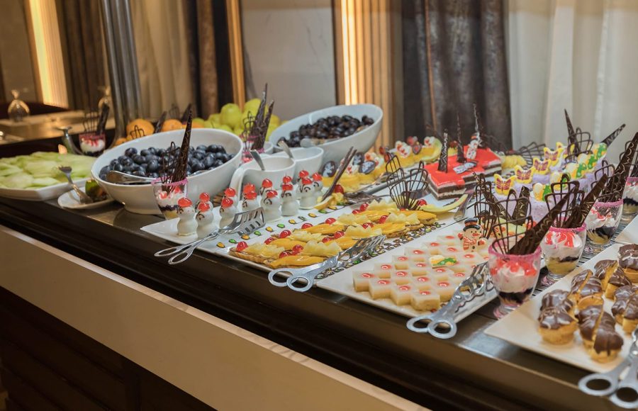 Buffet table featuring a rich array of colorful desserts, pastries, small cakes, and fresh fruit like grapes and melon.