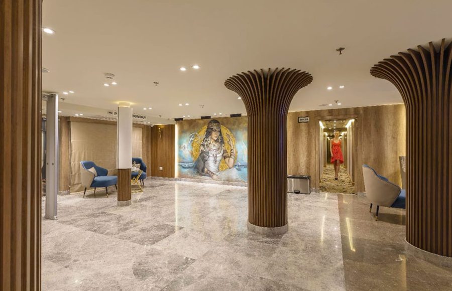 Cruise ship reception area with a central mural of an Egyptian figure, fluted wooden columns, and shiny gray marble floors.