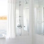A bright, all-white bathroom on a Nile Dahabiya boat featuring a pedestal sink and shower with a window overlooking the river.