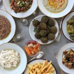 A top-down view of a large silver tray filled with various traditional Egyptian breakfast dishes like falafel, foul, and fresh salad.