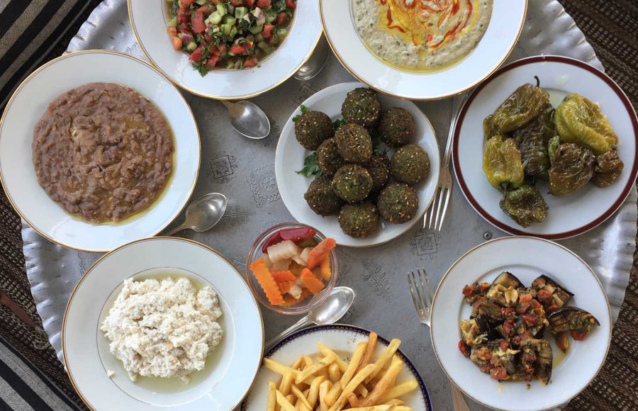 A top-down view of a large silver tray filled with various traditional Egyptian breakfast dishes like falafel, foul, and fresh salad.