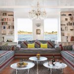 Elegant lounge area on a Nile Dahabiya boat featuring striped sofas, silver coffee tables, and large windows overlooking the river.