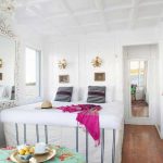 Bright, white panoramic suite on a Nile Dahabiya boat featuring a large bed, striped pillows, and a window view of the river.