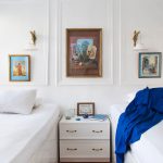 Two white twin beds in a cabin with framed art, wall lamps, and a white nightstand.