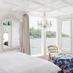 Bright, white luxury cabin on a Nile boat with a bed, ornate mirror, and panoramic windows.