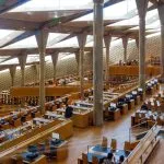 The ultra-modern, spacious main reading area of the Alexandria Library, featuring towering angled columns and tiered rows of desks.