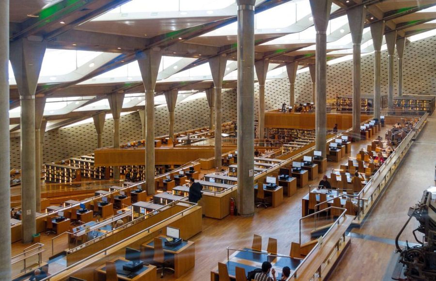 The ultra-modern, spacious main reading area of the Alexandria Library, featuring towering angled columns and tiered rows of desks.