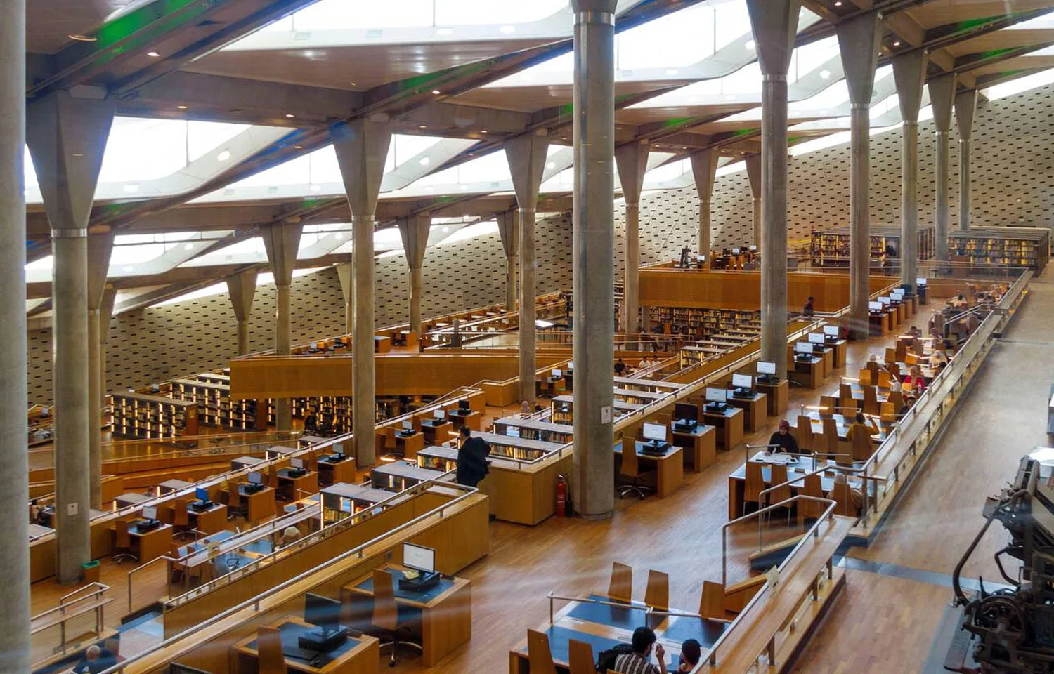 The ultra-modern, spacious main reading area of the Alexandria Library, featuring towering angled columns and tiered rows of desks.