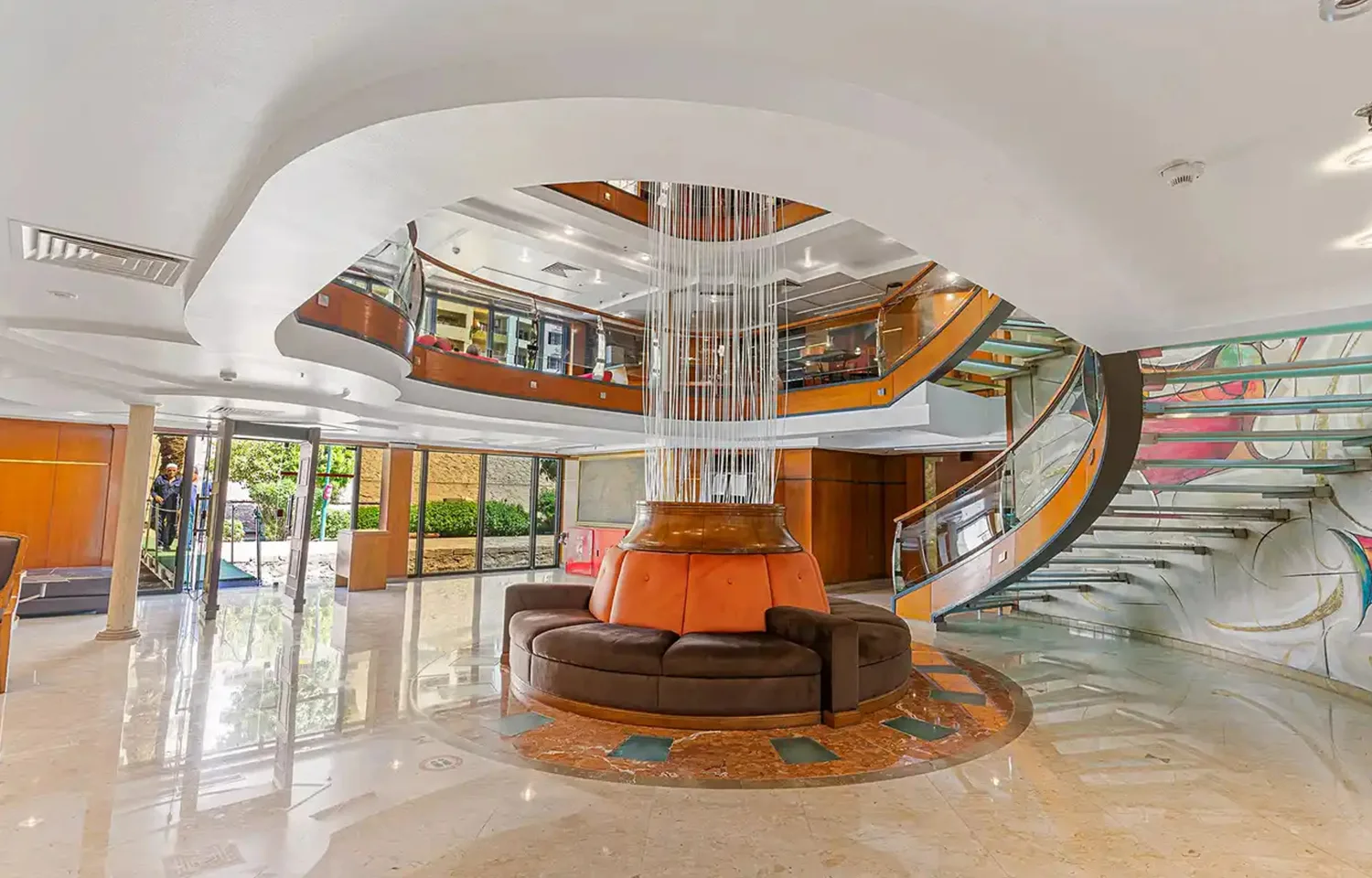 Indoor cruise ship salon with plush seating, central wooden bar, and red accents.