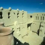 The distinctive, unpainted mud-brick courtyard of the Museum Of Badr In The Farafra Oasis Egypt, featuring unusual stylized human and animal relief sculptures and large clay pots.