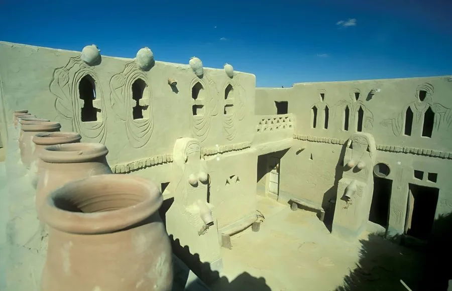 The distinctive, unpainted mud-brick courtyard of the Museum Of Badr In The Farafra Oasis Egypt, featuring unusual stylized human and animal relief sculptures and large clay pots.