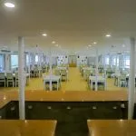 A wide-angle view of the Nile Palace Restaurant, showing the dining hall from the perspective of a serving counter, with rows of white tables and chairs and large windows overlooking the Nile.