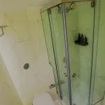 A modern cruise cabin bathroom with a corner glass-enclosed shower, a white toilet, and walls covered in light marble-look tiles with gold veining.