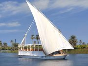 Nora Dahabiya Nile Cruise boat sailing on the water past palm trees.