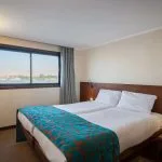 A comfortable, bright guest cabin on the cruise ship featuring two separate twin beds pushed together, a modern wooden headboard, and a large window with a view of the Nile.