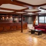 The lobby lounge and reception area of the MS Odyssey, featuring a dark wood reception desk, comfortable armchairs, a red sofa, and a large window overlooking the Nile.