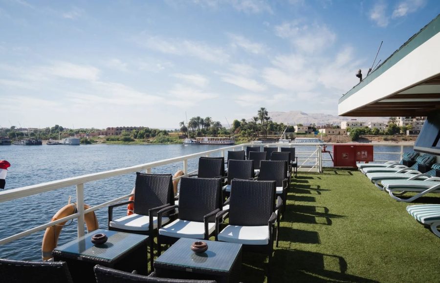Full side view of the MS Nile Odyssey cruise ship sailing on the river under a blue sky with dramatic white clouds.
