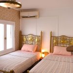 An elegant twin cabin on a Dahabiya Nile cruise featuring brass bed frames, floral wallpaper, and a window view.