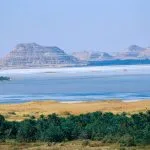 An aerial Overview of Siwa Oasis in Egypt Western Desert, showing the contrast between the green palm groves, the vast salt lake, and the distant, rocky mountains.