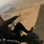 A close-up view of a tourist enjoying a paramotor over the pyramids during golden hour