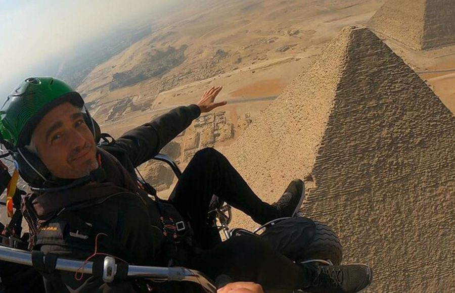 A close-up view of a tourist enjoying a paramotor over the pyramids during golden hour