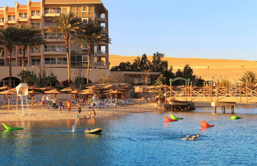 People enjoying the beach area with sun shades and lounging chairs at a resort on the Red Sea, showing a sunny hotel and resort area, perfect for the beach portion of a cairo luxor hurghada tour.