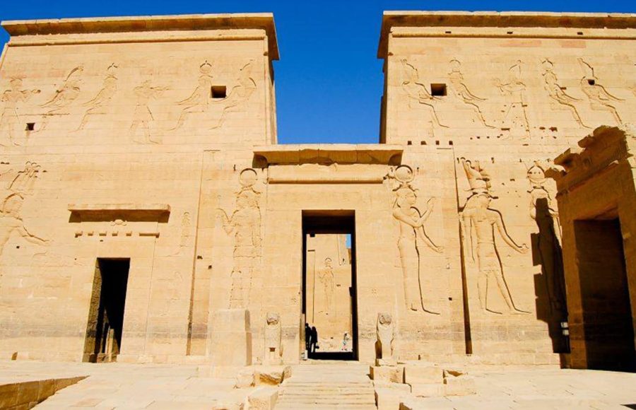 Facade of Philae Temple, Aswan, Egypt. Large stone entrance pylon with carved reliefs of pharaohs and gods under a bright blue sky.