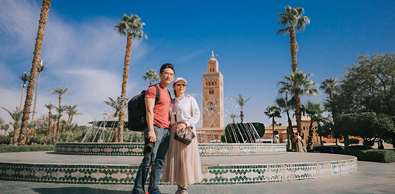 Portrait Asian Chinese tourist couple looking at camera in front of fountain Koutoubia Mosque