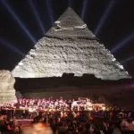 A live orchestra performs in front of the Cairo evening pyramids show with dramatic white light beams reaching into the night sky
