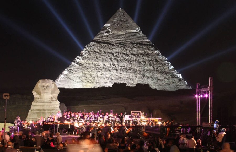 A live orchestra performs in front of the Cairo evening pyramids show with dramatic white light beams reaching into the night sky