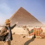A traveler enjoying a guided tour to pyramids and Cairo museum while standing next to a resting camel at Giza