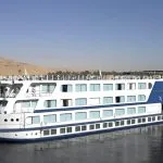 White and blue Nile cruise ship sailing past a sandy bank.