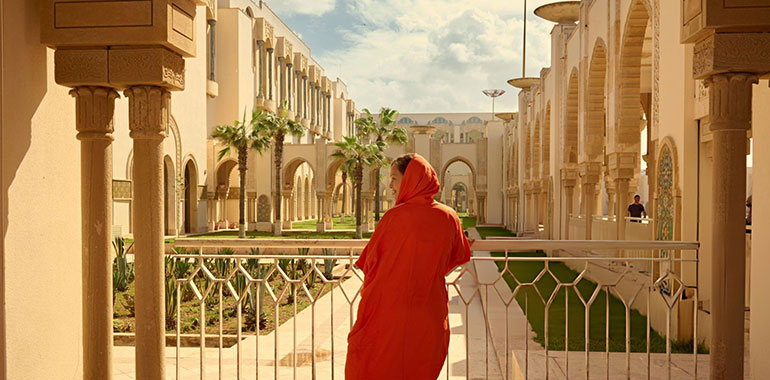 Rear view of a female tourist in traditional authentic Moroccan clothes visiting and admiring Hassan II mosque