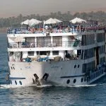 A large, multi-story River Nile Cruise ship River Nile Egypt Africa floats on blue water, a key part of any 12 days egypt tour.